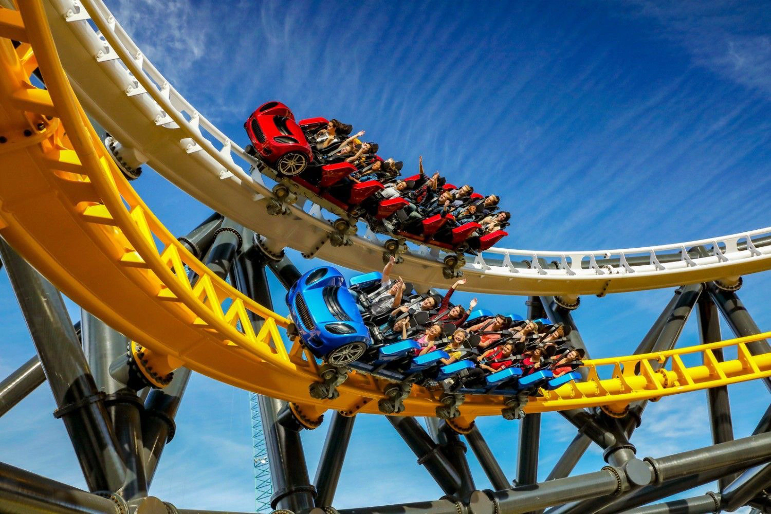Riders throw their hands up as red and blue West Coast Racers cars bank through yellow and white track