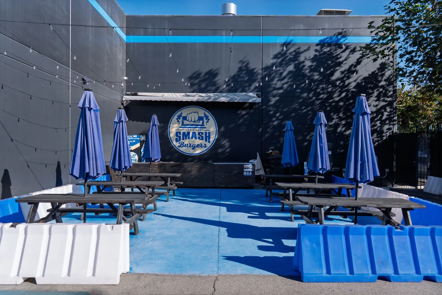 West Coast Smash outdoor patio with blue umbrellas and picnic tables